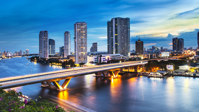 Thailand: Foto einer Brücke über den Fluss Chao Phraya in Bangkok, die Brücke ist beleuchtet und im Hintergrund stehen Häuser und Hochhäuser Thailand: Foto einer Brücke über den Fluss Chao Phraya in Bangkok, die Brücke ist beleuchtet und im Hintergrund stehen Häuser und Hochhäuser