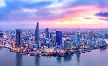 Vietnam: Luftaufnahme während des Sonnenunterganges von Ho Chi Minh City mit vielen Gebäuden im Vordergrund ist der Fluss Saigon zu sehen 