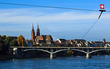 Schweiz: Panoramabild  von der Altstadt von Basel, Blick über den Rhein zu einer Brücke, schweizer Flagge oben recht
